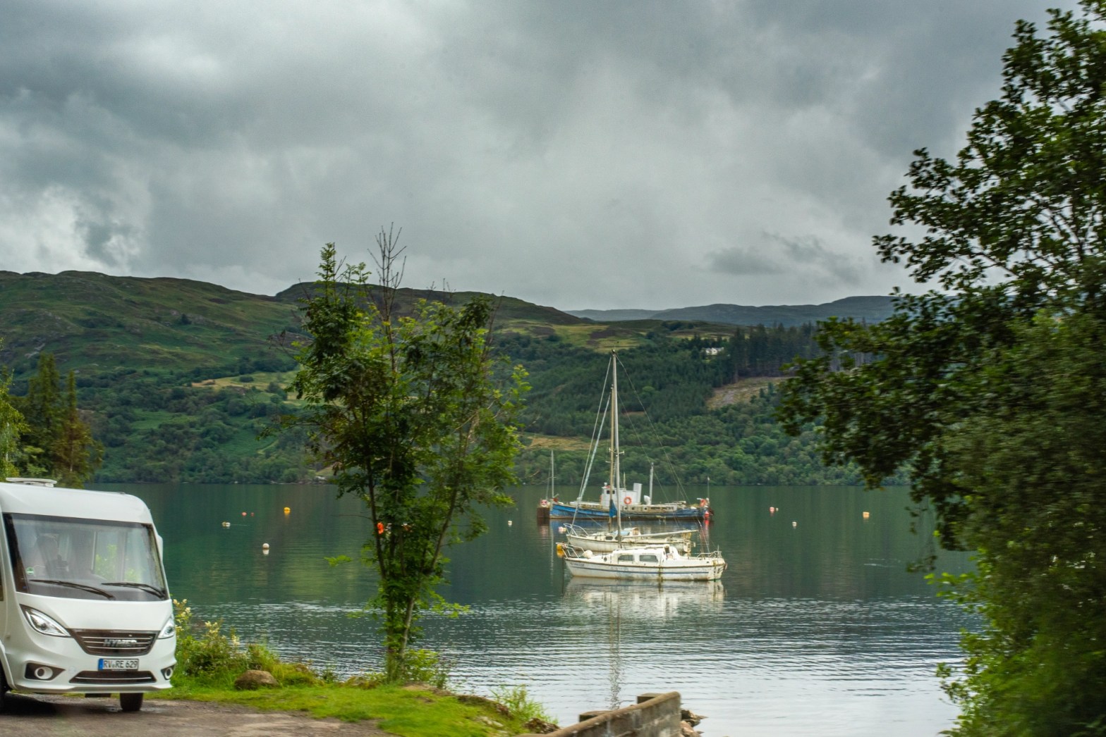 A view of 3 fishing boats moored on the Loch Ness. A motorhome sits in the layby.