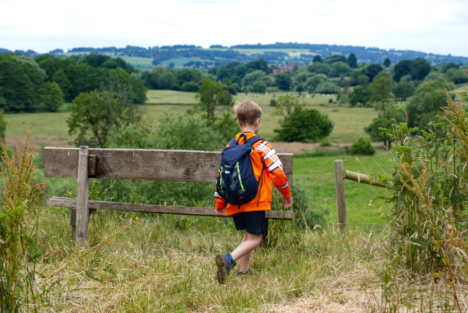 A boy with a backpack walking past a bench at Ford Hall Farm overlooking views of shropshire