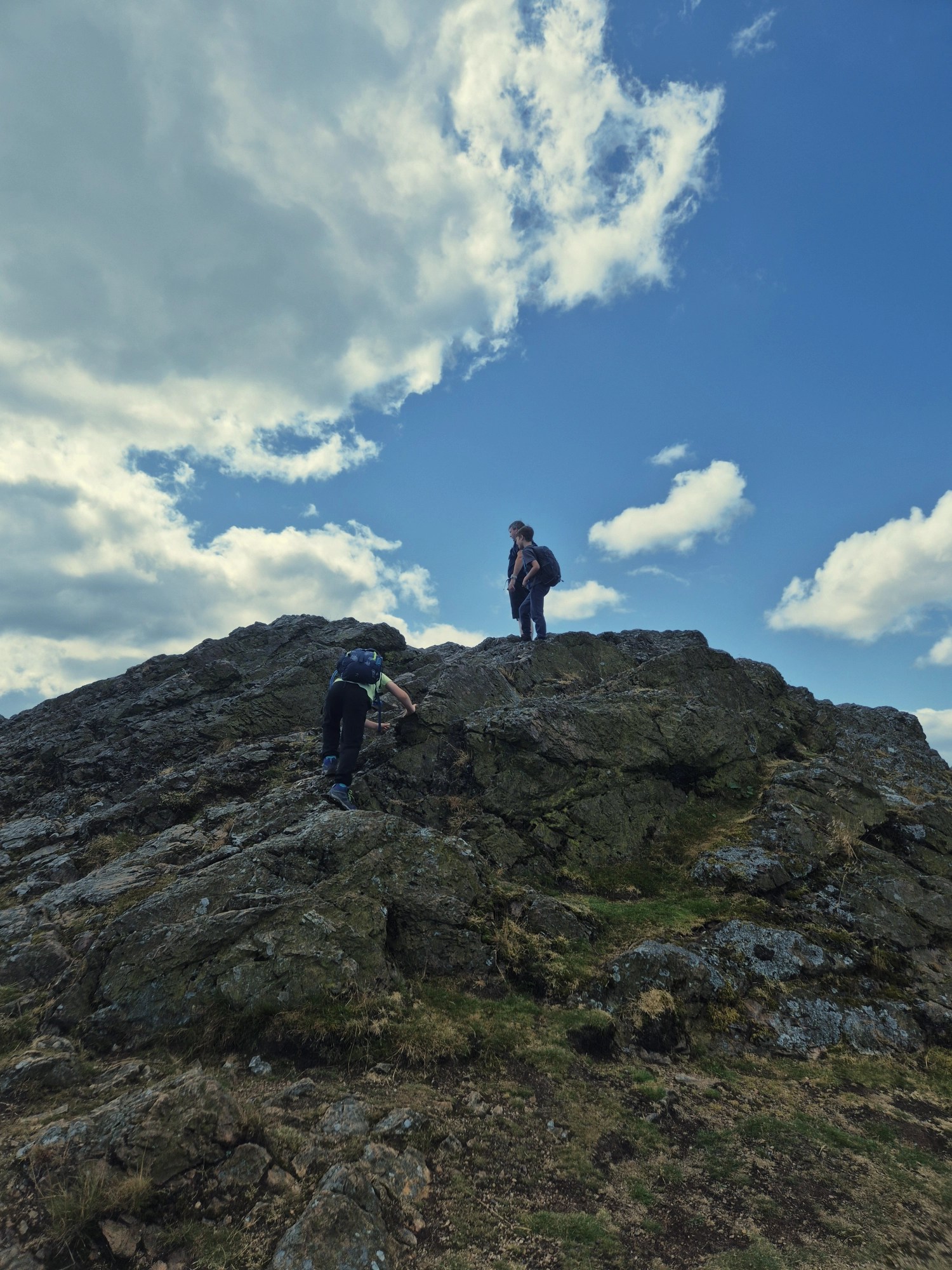 2 boys and a man scramble up some large rocks