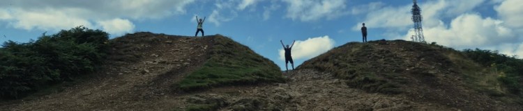 2 boys and a man wave their hands against a blue, cloudy skyline
