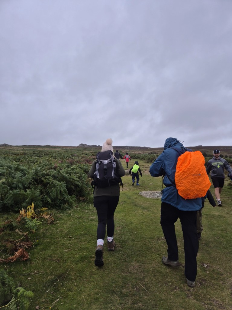 A group of people in wet weather gear scale a hill towards Stiperstones rocks