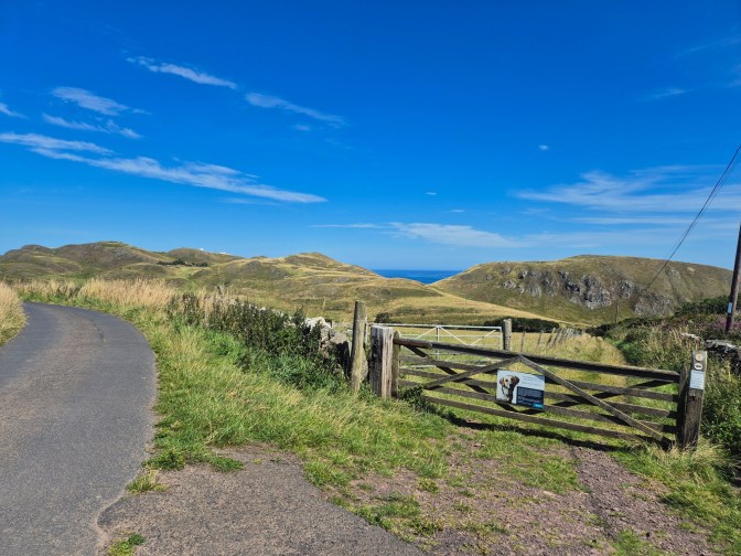 looking across fields with the ocean in the background and a wooden gate in the foreground