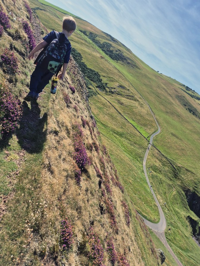 a boy walks along a narrow edge along a cliff