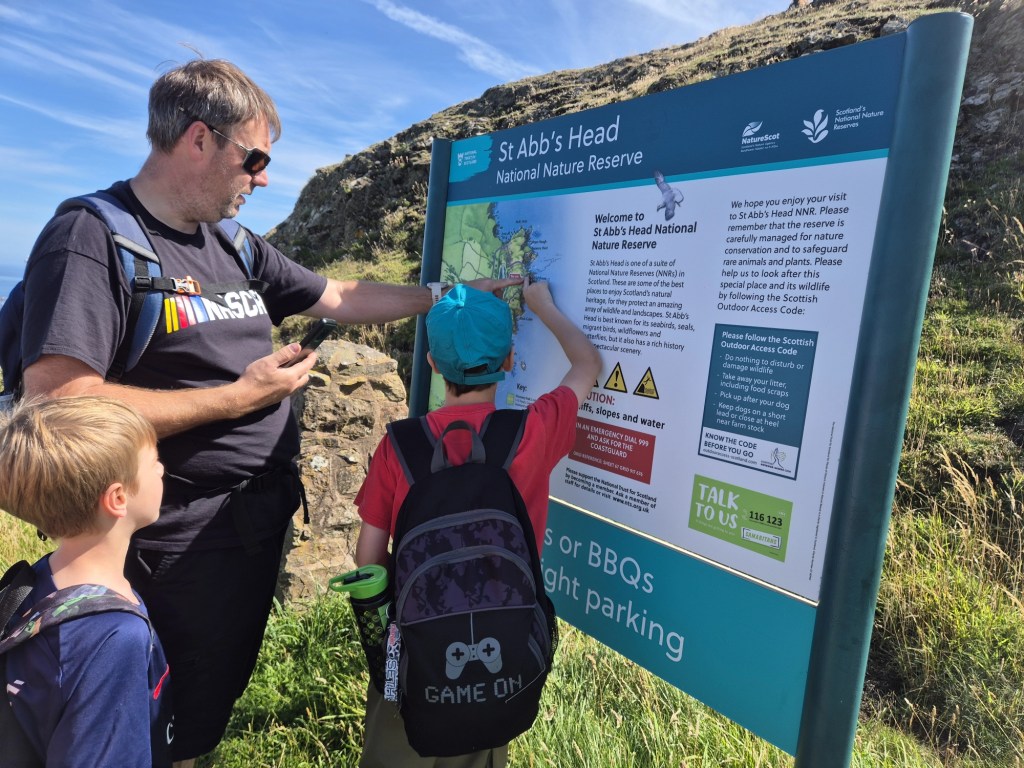 2 boys and a man read a sign for St Abbs Head Nature Reserve