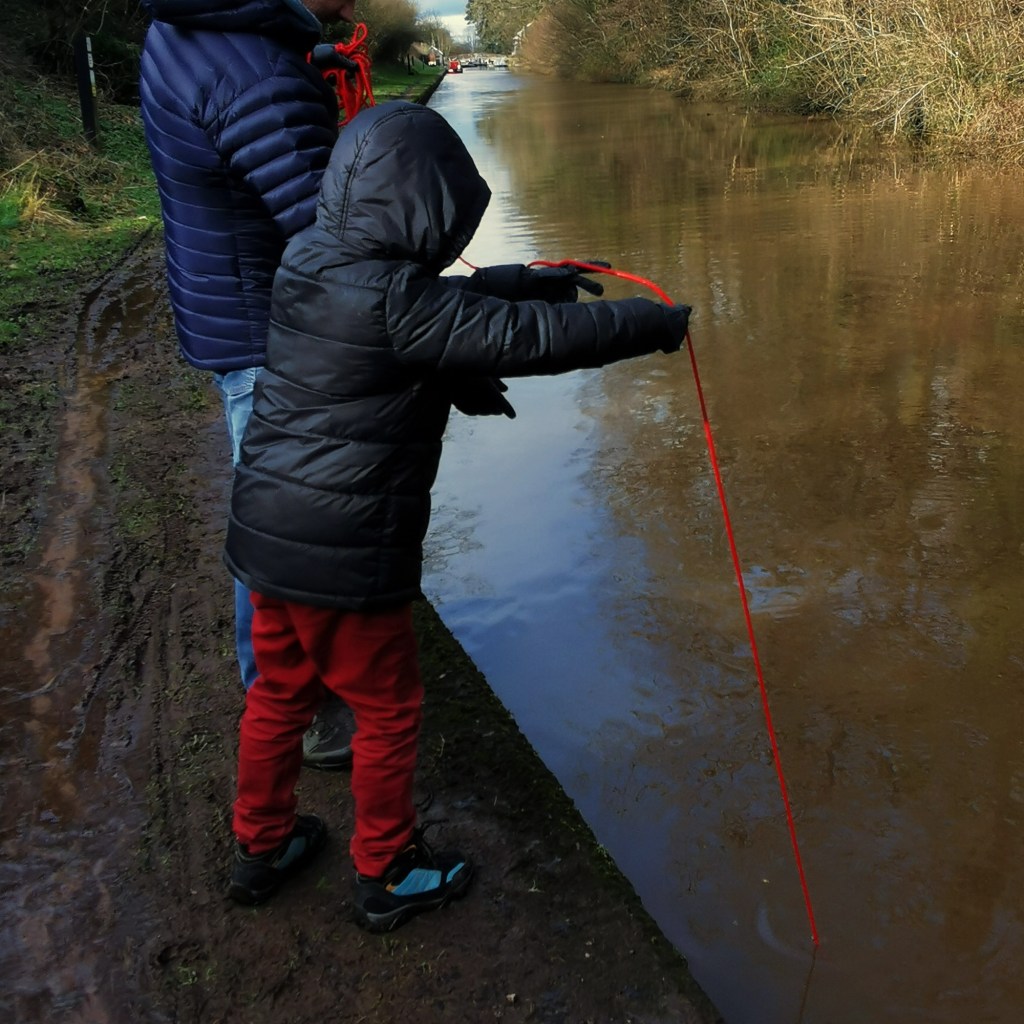 A man and a child carefully pull out their magnet from a canal towpath