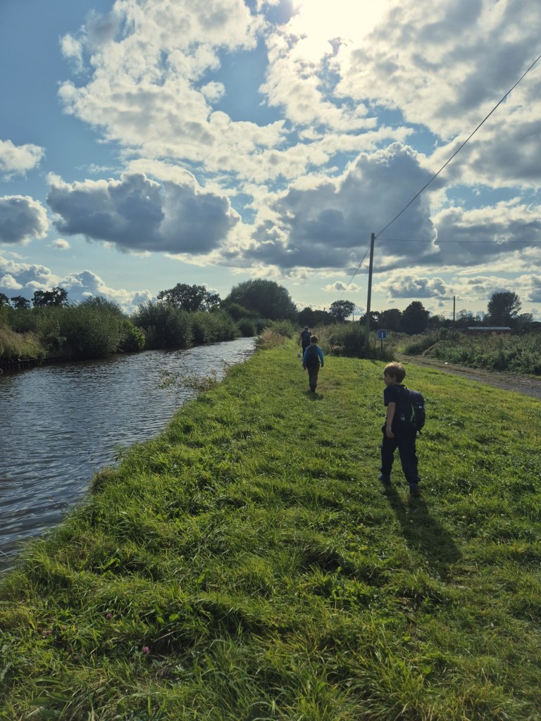 2 boys and a man walk beside a canal on a grassy towpath