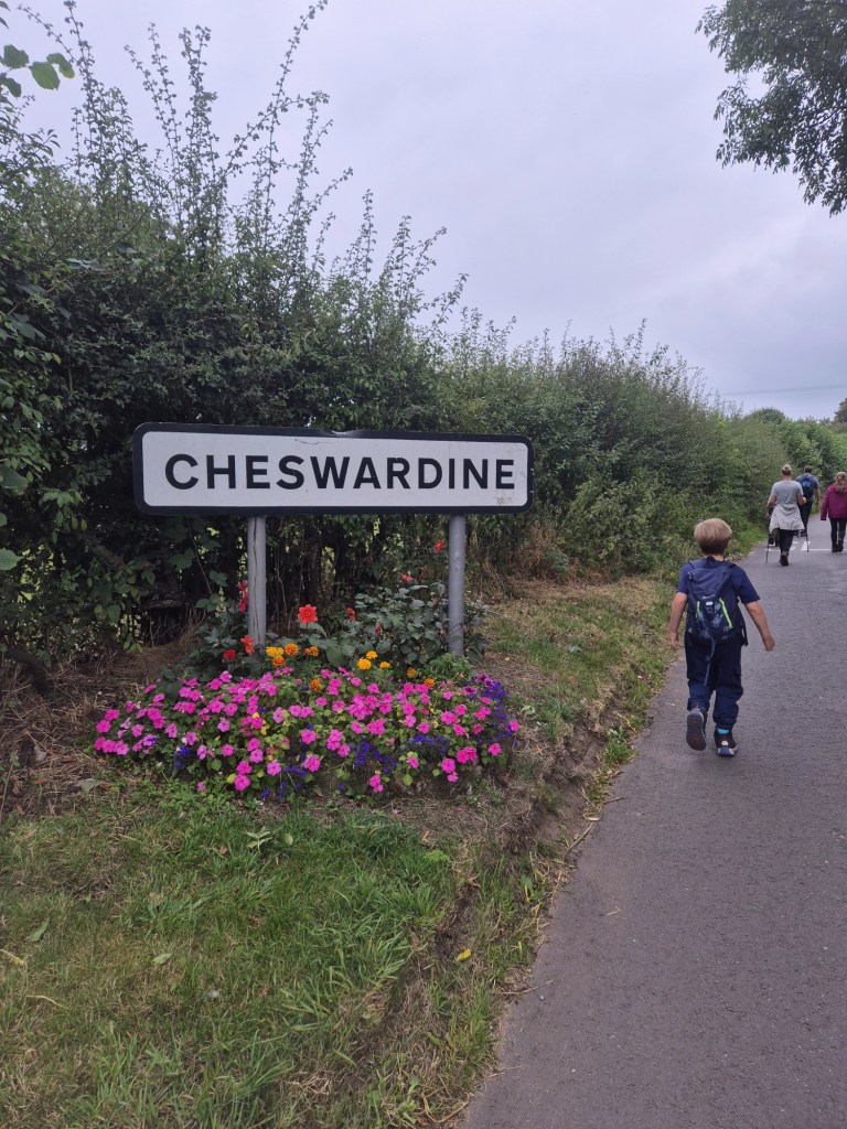 a boy walks past a village sign CHESWARDINE surrounded by pretty colourful flowers