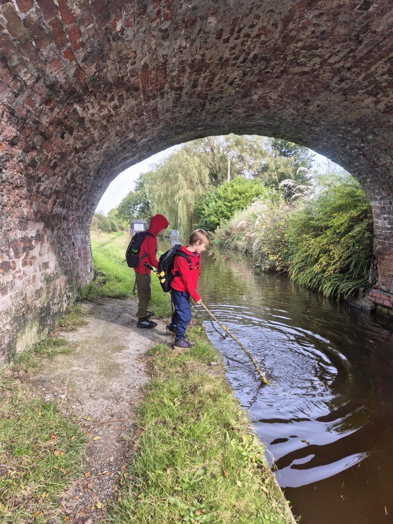 2 boys play with a stick under a canal bridge in the water