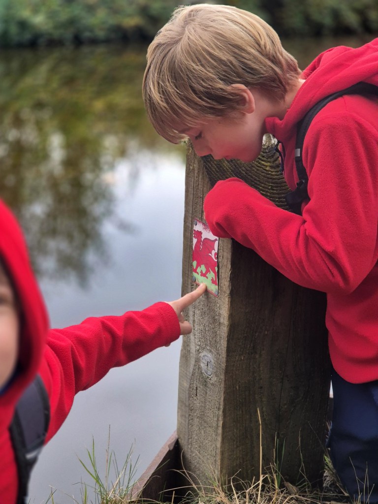 2 boys point at a wales flag on a post beside the canal