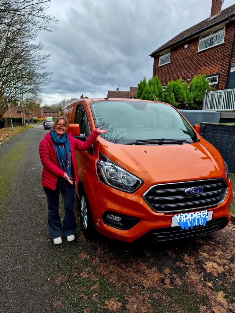 Woman stands next to a burnt orange transit van