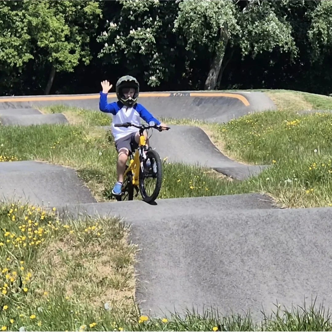 Boy on a mountain bike waving as he rides over rollers at a pump track