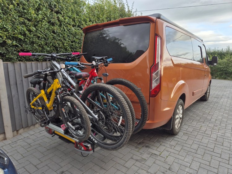 An orange ford transit van custom campervan conversion fitted with an atera strada evo 3+1 bike rack, fitted with 4 various sized bikes