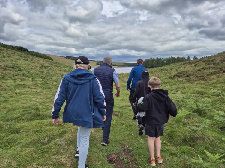 Family walking towards the low water shoreline at Whiteadder Reservoir on a cloudy day