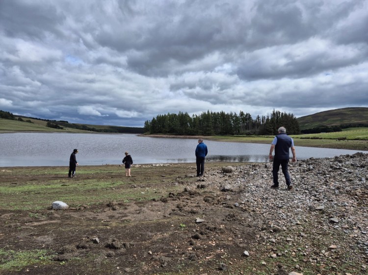 Family walking across the muddy reservoir bed towards the exposed shore