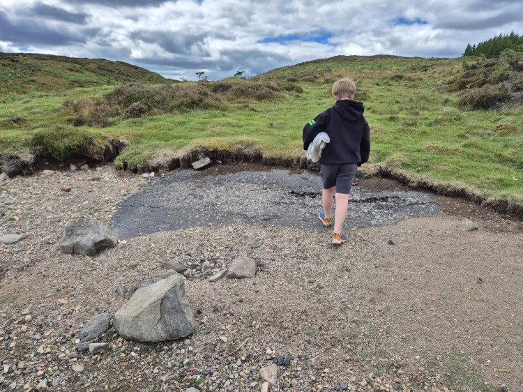 Person walking across pebbled shoreline at Whiteadder Reservoir with water receded
