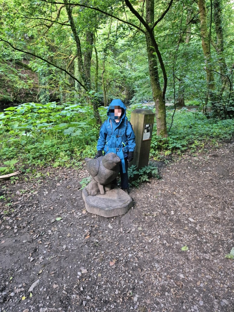 Child standing next to a carved animal sculpture on a forest trail