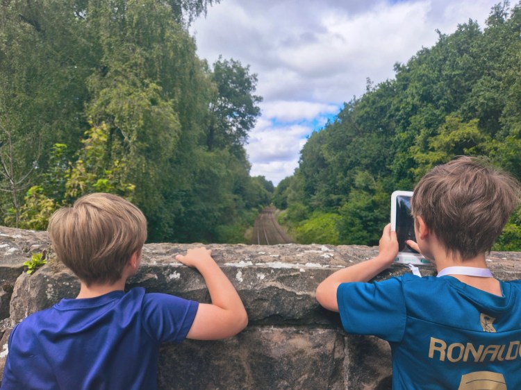 Boy taking a photo over a railway bridge at Delamere Forest, blue skies above