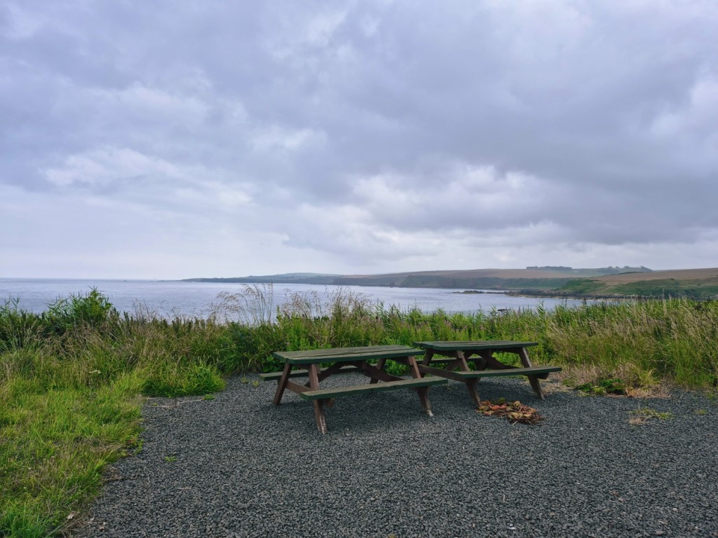 Picnic bench overlooking the sea under a cloudy sky.