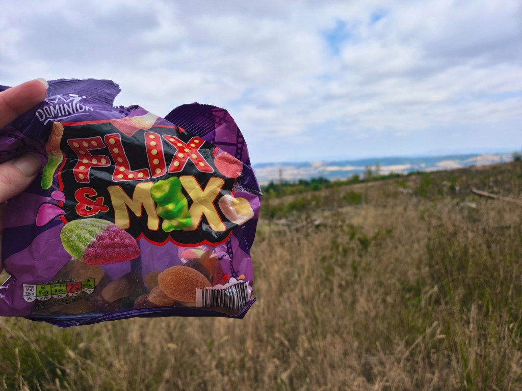 Bag of Flix Mix sweets held up against a countryside view – our mountain biking trail bribe of choice.