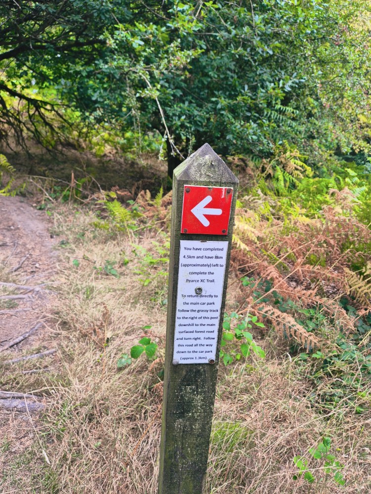 Red route trail marker post with arrow sign and warning notice at Hopton Woods