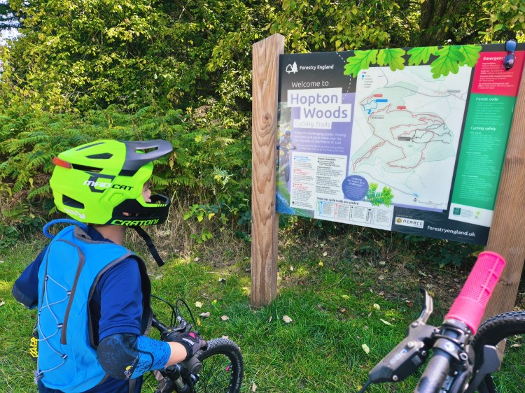 Child in a bright green helmet reading the Hopton Woods MTB trail information board.