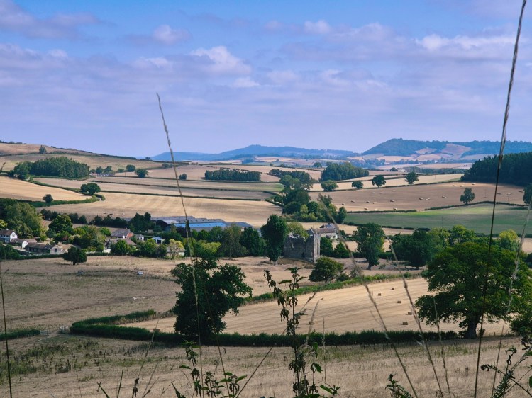 Panoramic countryside view from the top of Hopton Woods MTB trail, with rolling fields, a castle and distant hills.