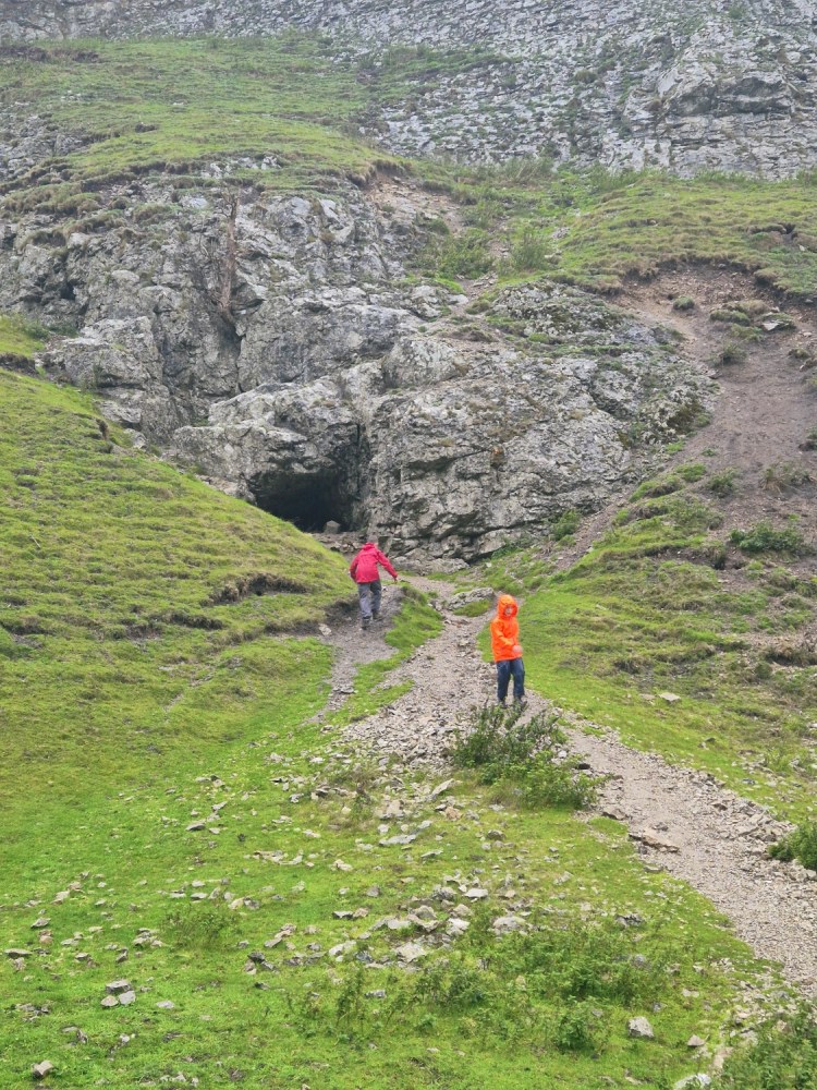 Family walking up a rocky trail between steep grassy hills in Castleton.