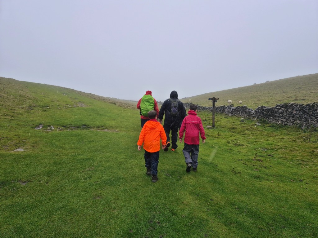 Family group walking across a misty hillside in bright waterproofs on a rainy day.