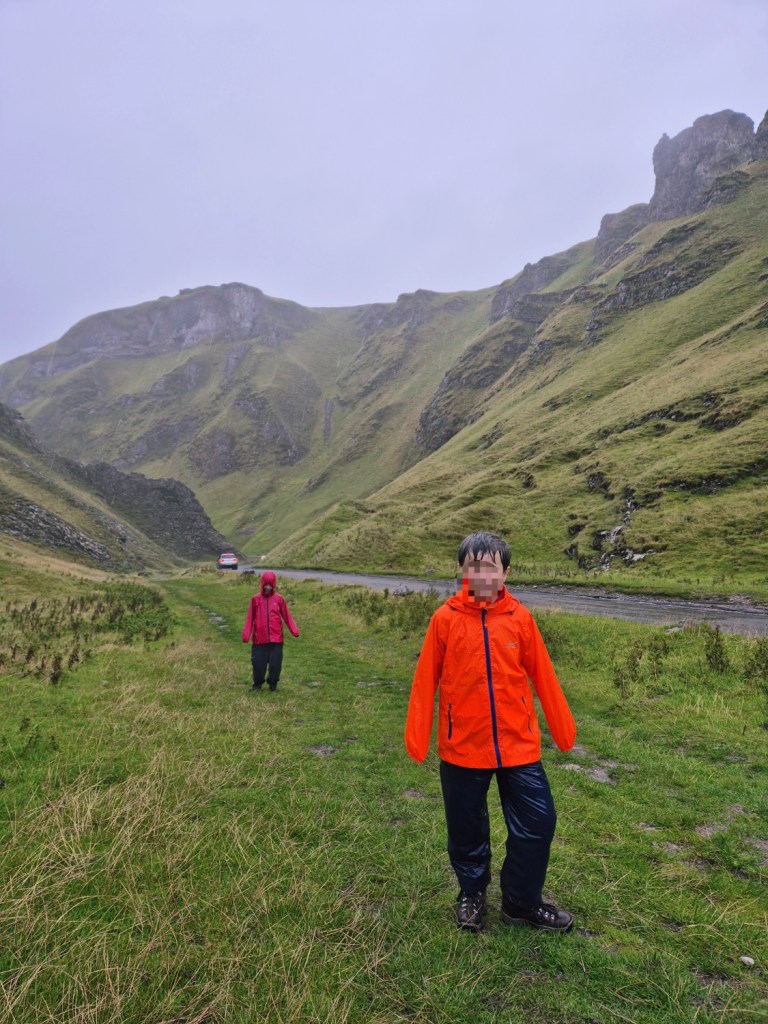 Boy in bright orange coat walking along a steep, dramatic gorge in the Peak District.