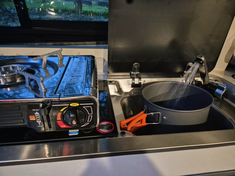 Camping stove set up inside a campervan kitchen, with pans and utensils ready for cooking a meal.